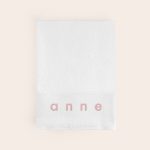 White personalised bath towel embroidered with the name Anne in pink thread.
