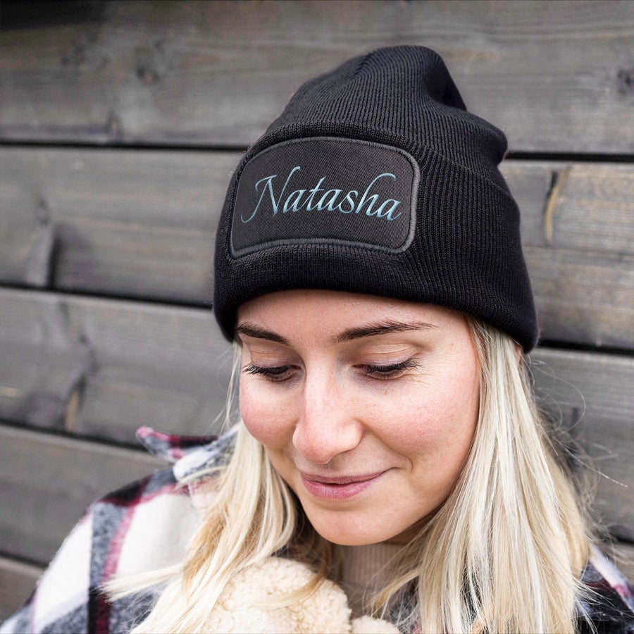Black beanie with the name Natasha embroidered in light blue on the front panel worn by a young woman