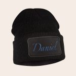 Black beanie with the name Daniel embroidered in blue on the front.