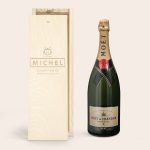 Moet & Chandon champagne bottle next to a wooden case engraved with "MICHEL" and "11.04.1990" on its lid.