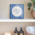 A personalized ceramic tile with a blue ornamental border and the proverb "There's no place like home - Rachel" printed in the center.