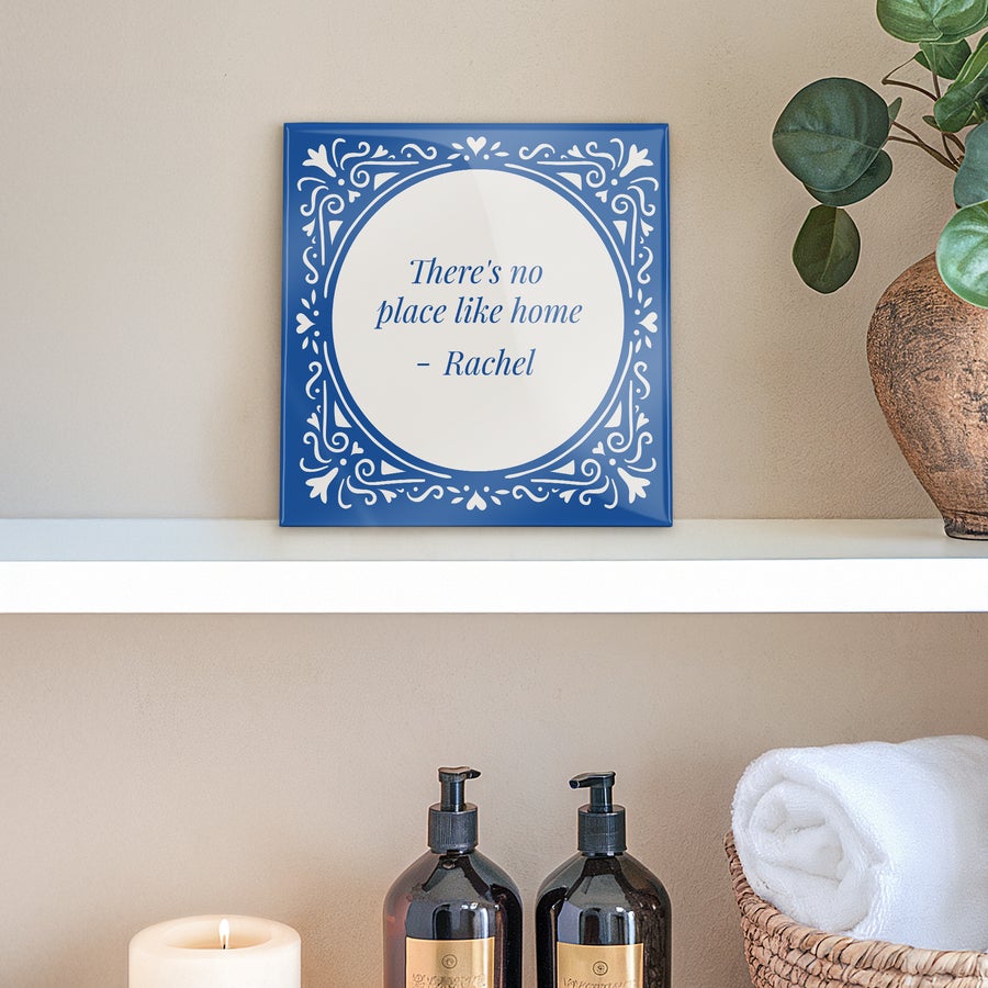 A personalized ceramic tile with a blue ornamental border and the proverb "There's no place like home - Rachel" printed in the center.