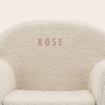 Close-up of a personalised kids teddy chair, showing the name ROSE embroidered in pink on the off-white fabric.