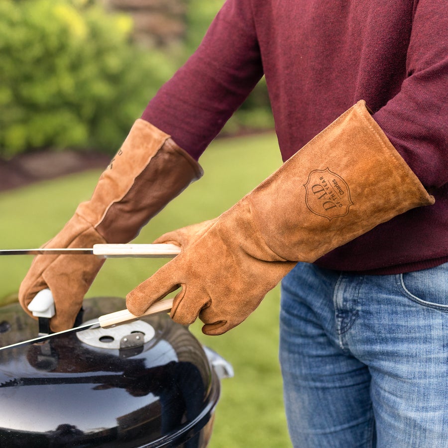 Person grilling with engraved leather BBQ gloves that read Dad of the Year Charles