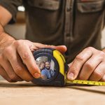 Personalised tape measure printed with a photo of a smiling couple, held by hands measuring on wood