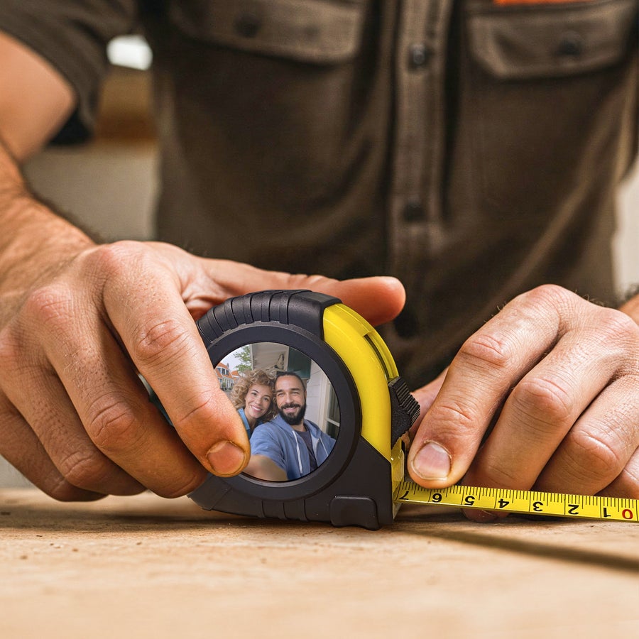 Personalised tape measure printed with a photo of a smiling couple, held by hands measuring on wood