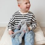 A smiling child holds a gray personalized Tiny Rabbit Richie cuddly toy with the name Vincent embroidered on its ear