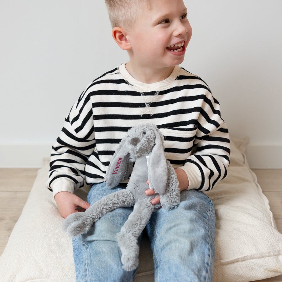 A smiling child holds a gray personalized Tiny Rabbit Richie cuddly toy with the name Vincent embroidered on its ear