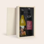 Wine gift set with two bottles of personalized wine in a wooden box. The white wine has a photo label with a couple and the text Cheers to Abena & Omari Just married. The red wine has a label with 2024 Abena & Omari.